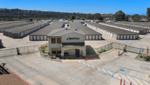 An aerial view of a Secure Storage facility shows rows of beige storage units, a two-story office at the entrance, and gated access with paved driveways.