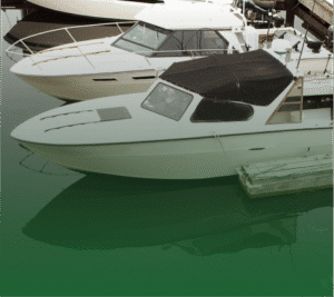 Photograph of several white boats docked in dark water. The closest boat has a black canvas cover over its cabin, and its reflection is visible in the water. A wooden dock is on the right.