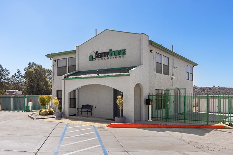 Resources-07 The Sentry Storage Solutions facility has a two-story beige stucco building with green trim, a gated entrance, and security fencing.
